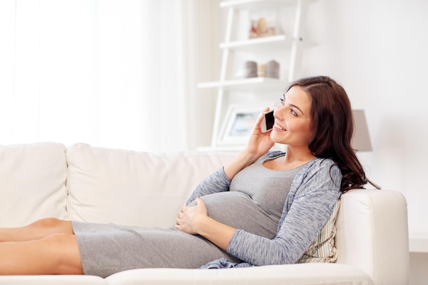 concepto de embarazo, maternidad, tecnología, personas y expectativas - mujer embarazada feliz llamando al teléfono inteligente en casa