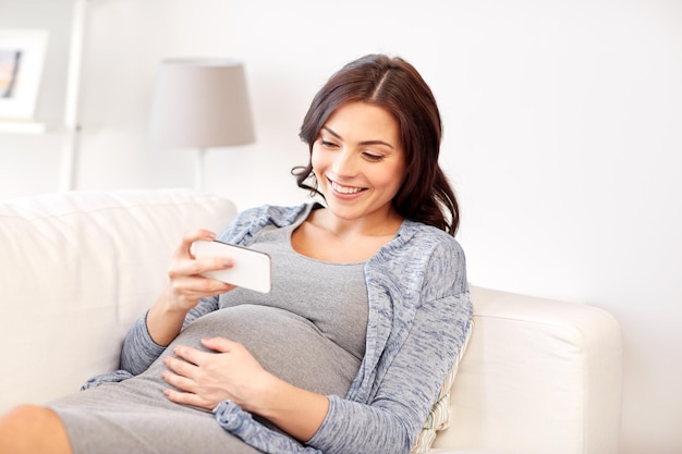 concepto de embarazo, maternidad, tecnología, personas y expectativas - mujer embarazada feliz con smartphone en casa