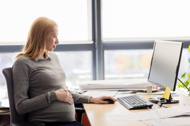 concepto de embarazo, negocios, trabajo y tecnología - mujer de negocios embarazada con computadora sentada en la mesa de la oficina