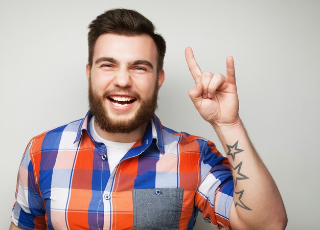 Concepto emocional y de personas: joven barbudo que muestra un gesto pesado sobre la superficie gris