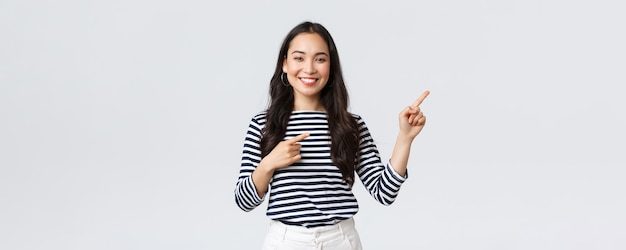 Concepto de emociones de la gente de la belleza y la moda de estilo de vida Mujer joven de buen aspecto con camisa a rayas señalando con el dedo a la derecha invitando a los clientes a anunciar un descuento especial sonriendo a la cámara feliz