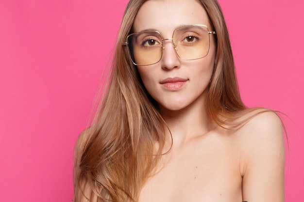 Concepto de emociones, moda, gente, juventud y belleza - Cierre de tiro de mujer joven con estilo en gafas de sol sonriendo sobre fondo rosa. Modelo de mujer hermosa con espacio de copia.