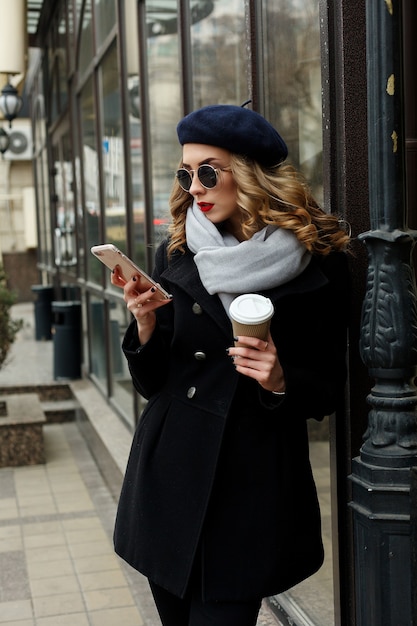 Concepto de emociones, personas, belleza y estilo de vida - Chica francesa. Foto de la calle mujer joven con ropa clásica con estilo. Concepto de moda femenina. Estilo francés. Chica enviando mensajes de texto al teléfono inteligente. café