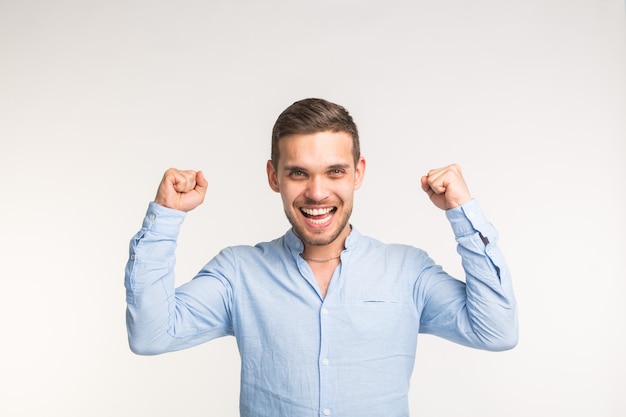 Concepto de emociones, victoria y personas - hombre alegre guapo con los brazos hacia arriba sobre la superficie blanca