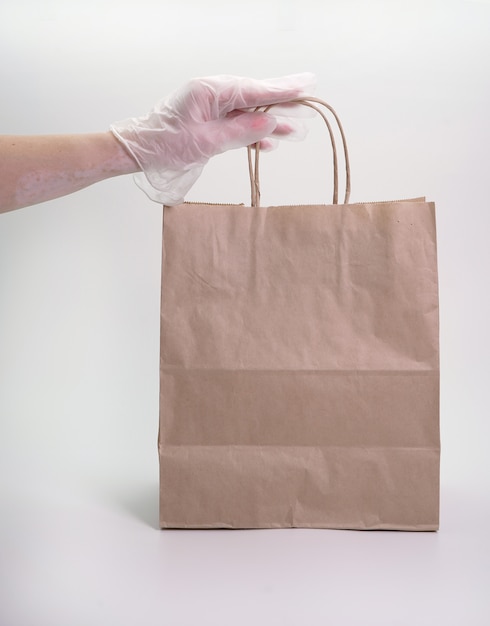 Concepto de entrega de alimentos preparados, la mano enguantada de una mujer sostiene una bolsa de papel con comida sobre un fondo blanco aislado