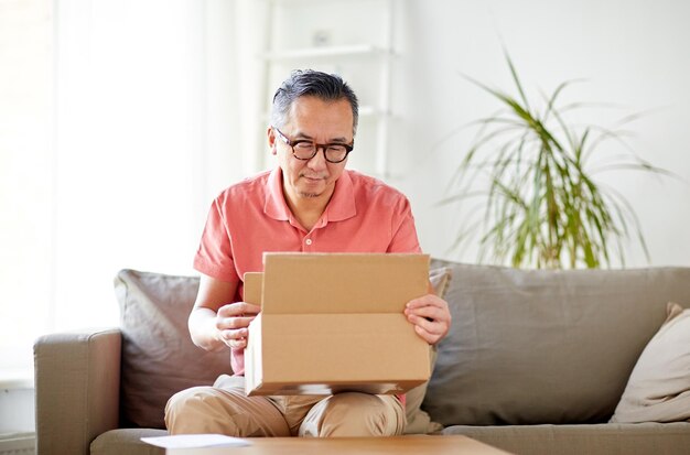 Foto concepto de entrega, correo, consumismo y personas - hombre abriendo una caja de paquetes en casa