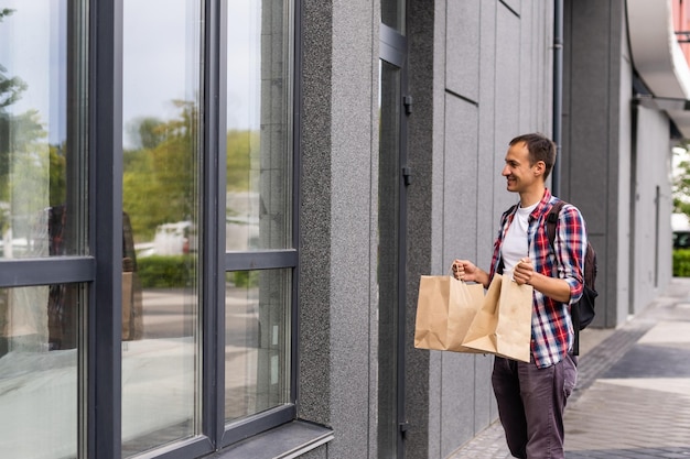 Concepto de entrega, correo y personas: hombre feliz entregando alimentos en una bolsa de papel desechable a la casa del cliente