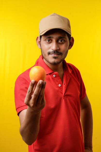 Concepto de entrega de frutas: repartidor indio con fruta naranja en la mano