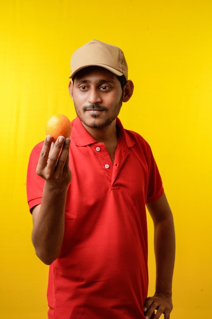 Concepto de entrega de frutas: repartidor indio con fruta naranja en la mano