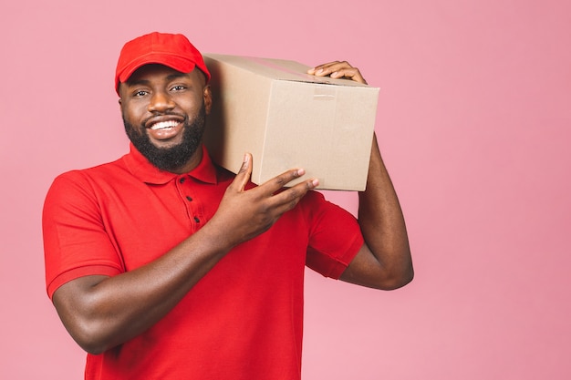 Concepto de entrega. Hombre negro afroamericano de entrega que lleva el paquete aislado sobre fondo rosa.