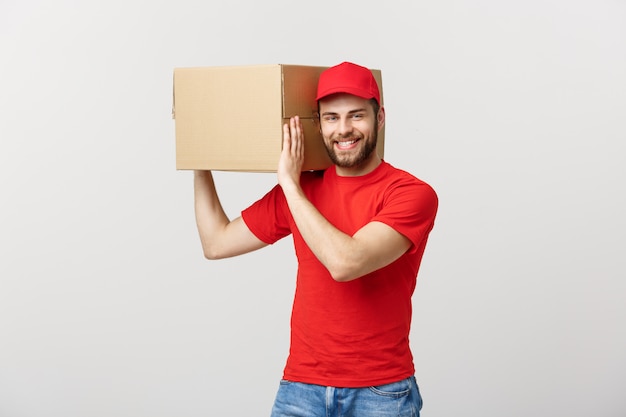 Foto concepto de entrega: joven caucásico guapo repartidor sosteniendo una caja en el hombro.