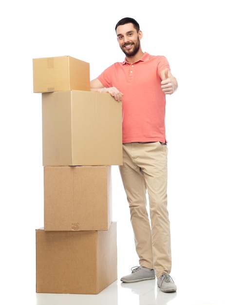 Foto concepto de entrega, mudanza, personas y logística - hombre feliz con un montón de cajas de cartón mostrando los pulgares hacia arriba