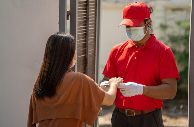 El concepto de entrega segura Un mensajero con uniforme rojo y máscara protectora entrega al cliente