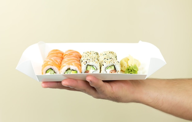 Foto concepto de entrega de sushi, hombre de mensajería con juegos de sushi en un recipiente de papel desechable