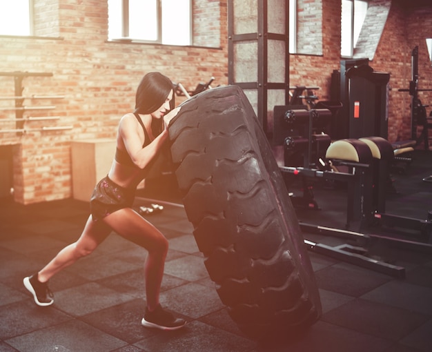 Concepto de entrenamiento funcional. Fuerte joven morena empujando una rueda pesada en el gimnasio.