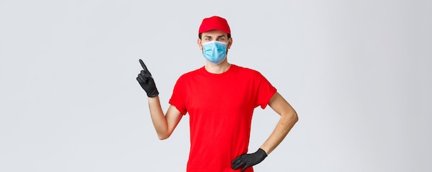 Concepto de envío y compras en línea de autocuarentena de covid19 Repartidor con gorra roja y máscara médica de camiseta con guantes para proteger a los clientes y empleados señalando con el dedo a la izquierda en el anuncio de promoción