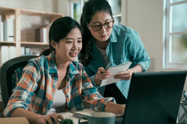 Concepto de equipo de inicio. dos mujeres de negocios discutiendo juntas mirando la computadora portátil en una oficina luminosa y acogedora. grupo de colegas hablando alegremente escuchando trabajando en un lugar de trabajo de estudio moderno.