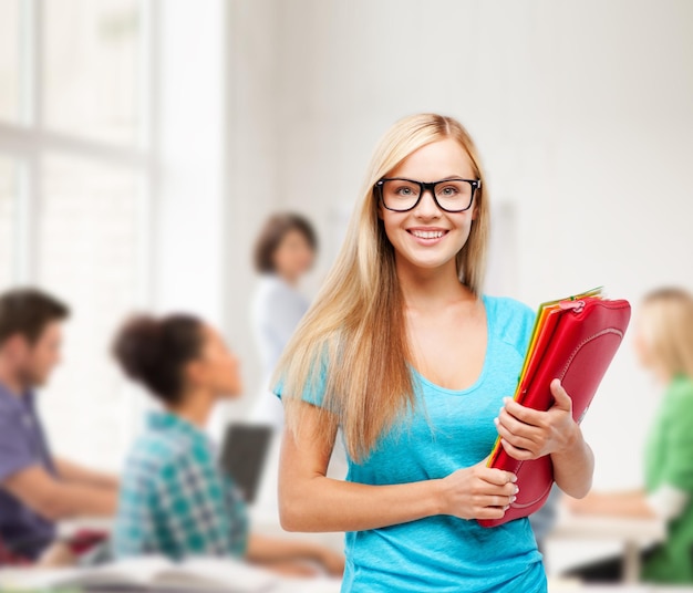 concepto de escuela y educación - estudiante sonriente en anteojos con carpetas