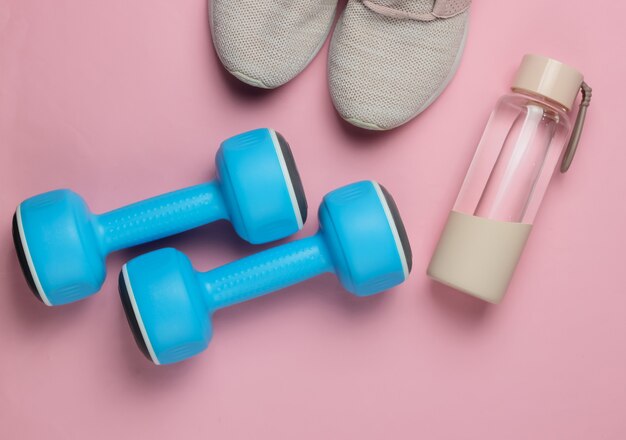 Concepto de estilo plano laico de estilo de vida saludable, deporte y fitness. calzado deportivo para correr, pesas, botella de agua sobre fondo rosa pastel. vista superior