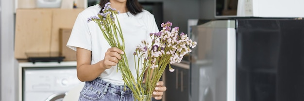 Concepto de estilo de vida acogedor Mujer joven flores frescas para decorar en jarrón sobre la mesa en la cocina