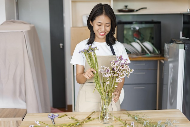 Concepto de estilo de vida acogedor Mujer joven flores frescas para decorar en jarrón sobre la mesa en la cocina