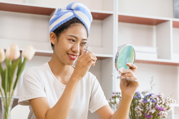 Concepto de estilo de vida acogedor Mujer joven en turbante después de la ducha y pestañas rizadas para maquillarse en casa