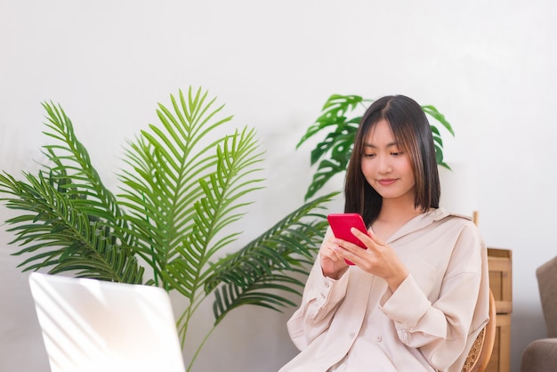 Concepto de estilo de vida en casa Mujer asiática sentada en una silla y usando un teléfono inteligente para navegar en las redes sociales