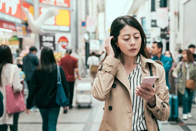 Concepto de estilo de vida. Cerca de una joven y encantadora mujer asiática con abrigo sonriendo charlando con su novio en un smartphone. señora de la oficina comprando y caminando en shinsaibashi y usando el teléfono celular hablando en línea.