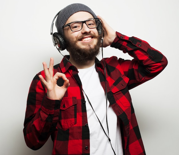 Concepto de estilo de vida, educación y personas: joven barbudo escuchando música mientras está de pie contra el fondo gris. Estilo hipster.