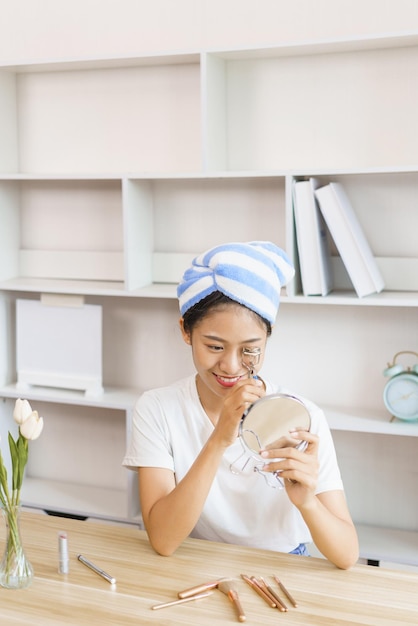 Concepto de estilo de vida en el hogar Mujer joven en turbante después de la ducha y pestañas rizadas para maquillarse en casa