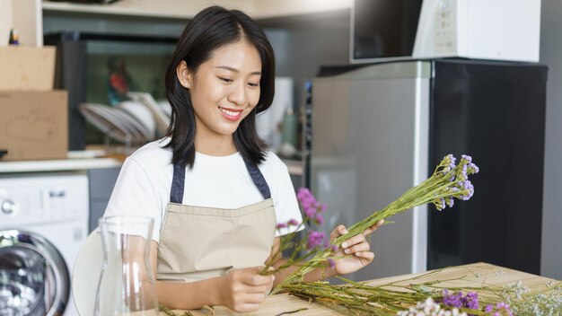 Concepto de estilo de vida hogareño Mujer joven sentada en la cocina y arreglando flores en un jarrón sobre la mesa