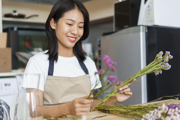 Concepto de estilo de vida hogareño Mujer joven sentada en la cocina y arreglando flores en un jarrón sobre la mesa