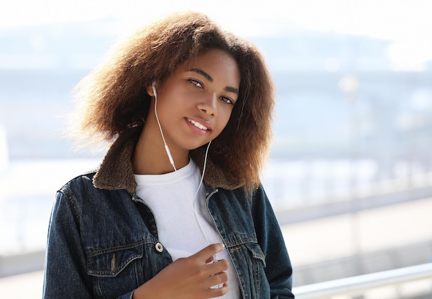 Concepto de estilo de vida Joven afroamericana usando teléfono móvil y auriculares sonriendo