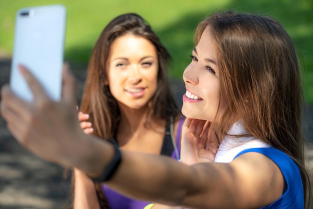 Concepto de estilo de vida de los millennials dos chicas deportivas tomándose un selfie y sonriendo después de entrenar al aire libre en un día soleado