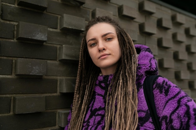 Concepto de estilo de vida una mujer joven con dreadlocks y piercings camina contra el fondo de un