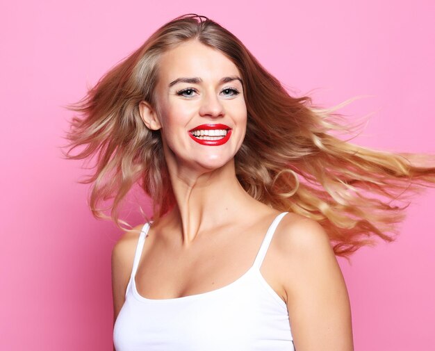 Concepto de estilo de vida y personas Joven linda chica rubia sonriente sobre fondo rosa