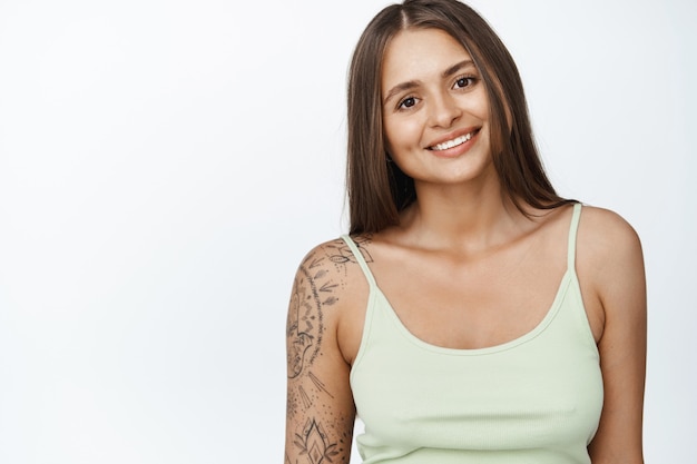 Concepto de estilo de vida de personas. Retrato de joven mujer moderna de 25 años, sonriendo y mirando feliz en blanco