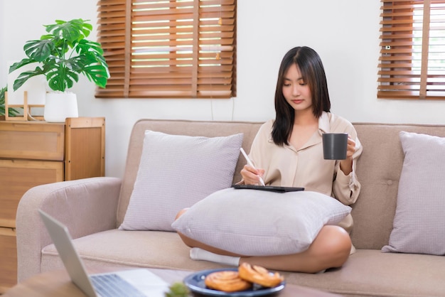 Concepto de estilo de vida de relajación Mujer asiática joven escribiendo y trabajando en tableta mientras bebe café