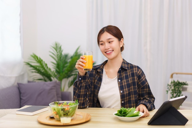 Concepto de estilo de vida en la sala de estar Mujer asiática bebiendo jugo de naranja y comiendo ensalada de verduras