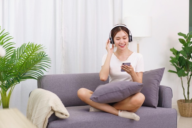 Concepto de estilo de vida en la sala de estar Mujer asiática joven en auriculares para escuchar música en el teléfono inteligente