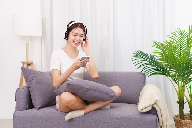 Concepto de estilo de vida en la sala de estar Mujer asiática joven en auriculares para escuchar música en el teléfono inteligente