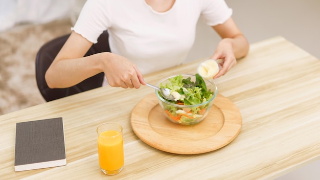 Concepto de estilo de vida en la sala de estar Mujer asiática joven mezclando ensalada de verduras con aderezo para ensaladas