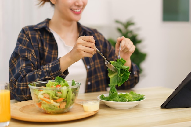 Concepto de estilo de vida en la sala de estar Mujer asiática joven mirando tableta y comiendo ensalada de verduras