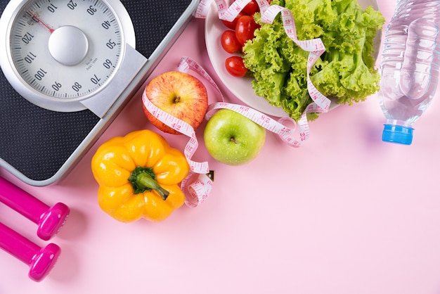 Concepto de estilo de vida saludable, comida y deporte sobre fondo rosa pastel.