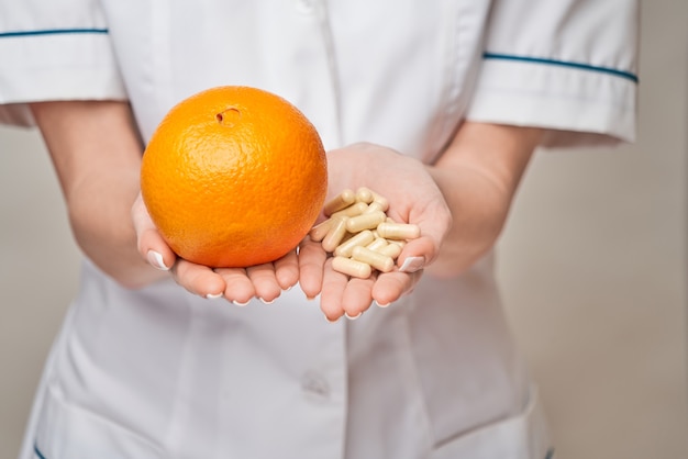 Concepto de estilo de vida saludable médico nutricionista - sosteniendo cápsulas o píldoras de vitamina de frutas y nutrición de naranja