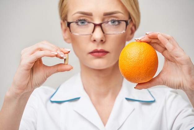 Concepto de estilo de vida saludable médico nutricionista - sosteniendo cápsulas de vitamina y fruta naranja orgánica fresca