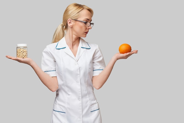 Concepto de estilo de vida saludable médico nutricionista - sosteniendo cápsulas de vitamina y fruta naranja orgánica fresca