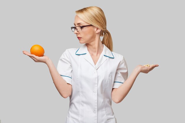 Concepto de estilo de vida saludable médico nutricionista - sosteniendo cápsulas de vitamina y fruta naranja orgánica fresca