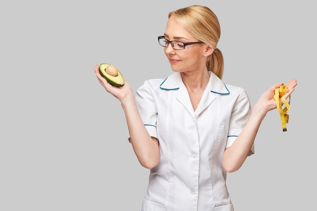 concepto de estilo de vida saludable médico nutricionista - sosteniendo fruta de aguacate orgánico y cinta métrica