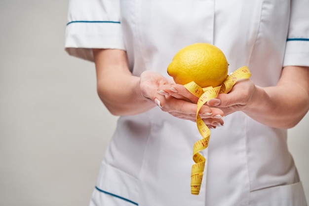 Concepto de estilo de vida saludable médico nutricionista - sosteniendo fruta de limón orgánico y cinta métrica.